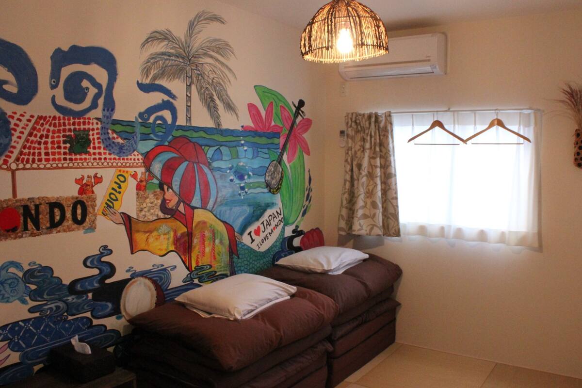 A room with a mural, a sofa, a hanging light fixture, and a window with curtains.
