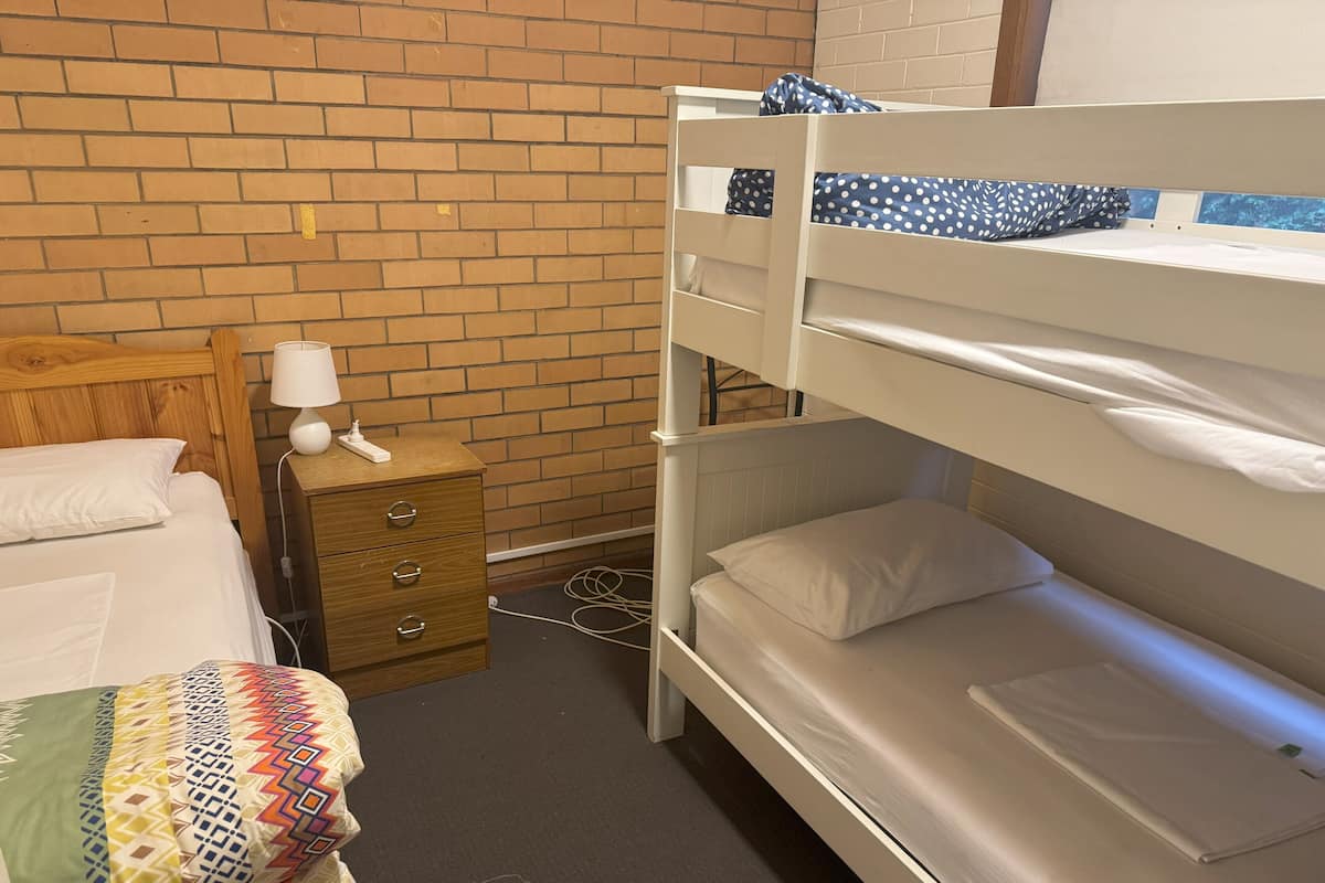 A bunk bed room with a wooden headboard, a bedside table with a lamp, and a patterned blanket.