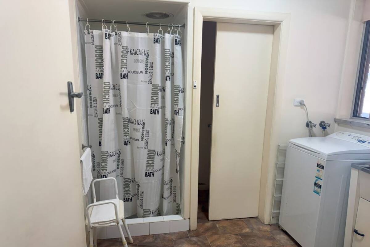 A bathroom with a shower curtain, a washing machine, and a small chair.