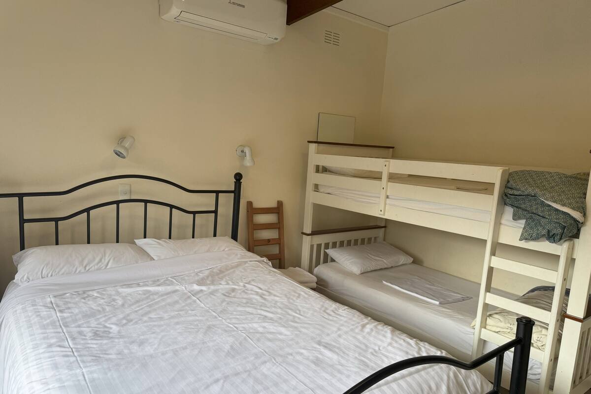 A bedroom with a single bed, a bunk bed, a bedside table, a lamp, and an air conditioning unit.