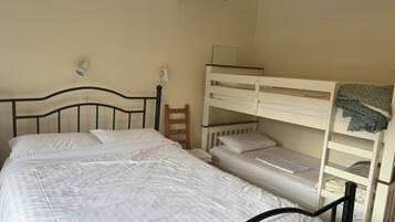 Une chambre avec un lit simple, un lit superposé, une table de chevet, une lampe et un appareil de climatisation.