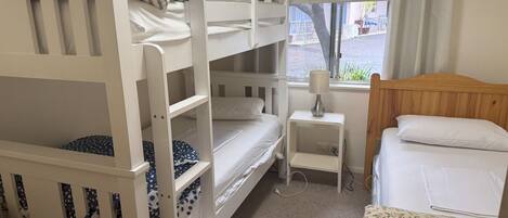 Una habitación con literas, una mesita de noche con lámpara, una ventana con cortinas y una cama con colcha estampada.