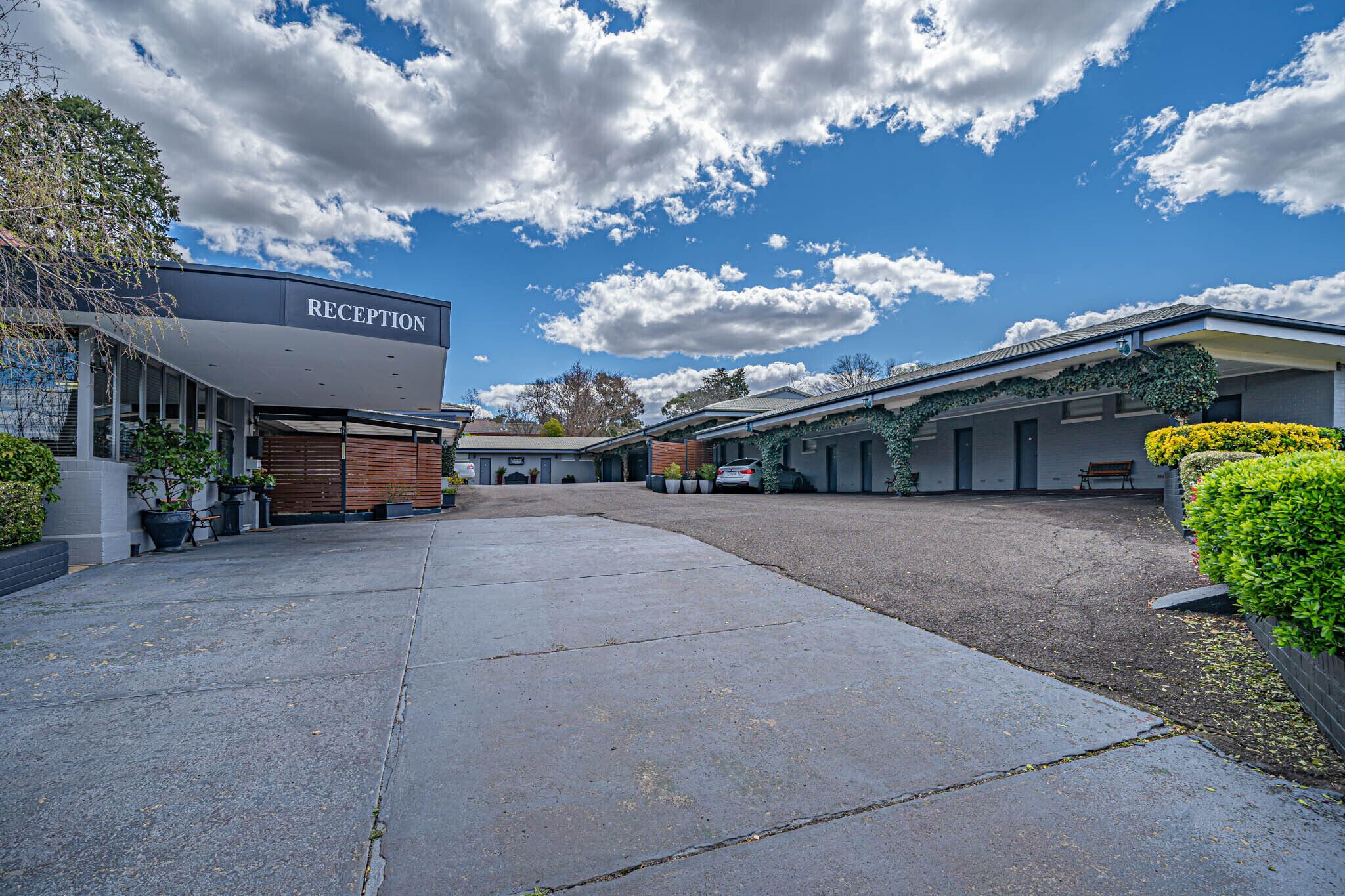 Zona de recepción con cielo despejado y nubes, un camino pavimentado y un edificio con un cartel que dice "RECEPTION".