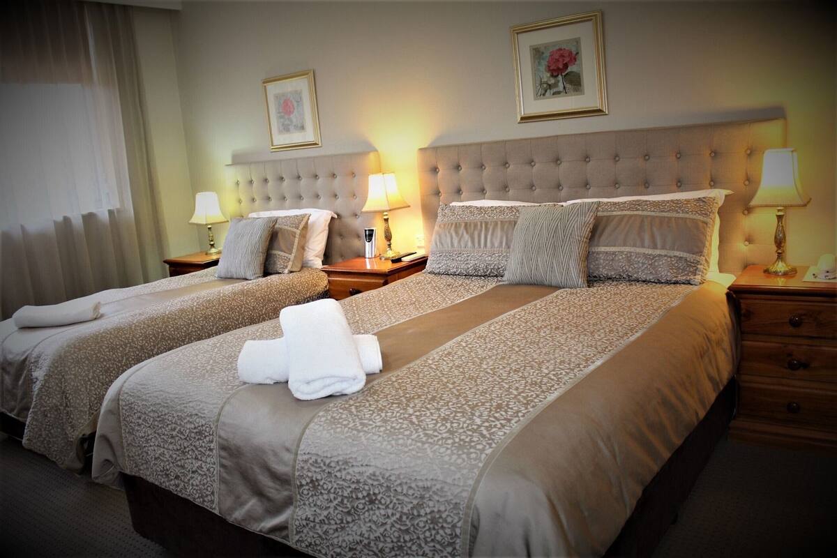 Una habitación de hotel con dos camas, un cabecero grande, lámparas de noche y una mesita de noche.