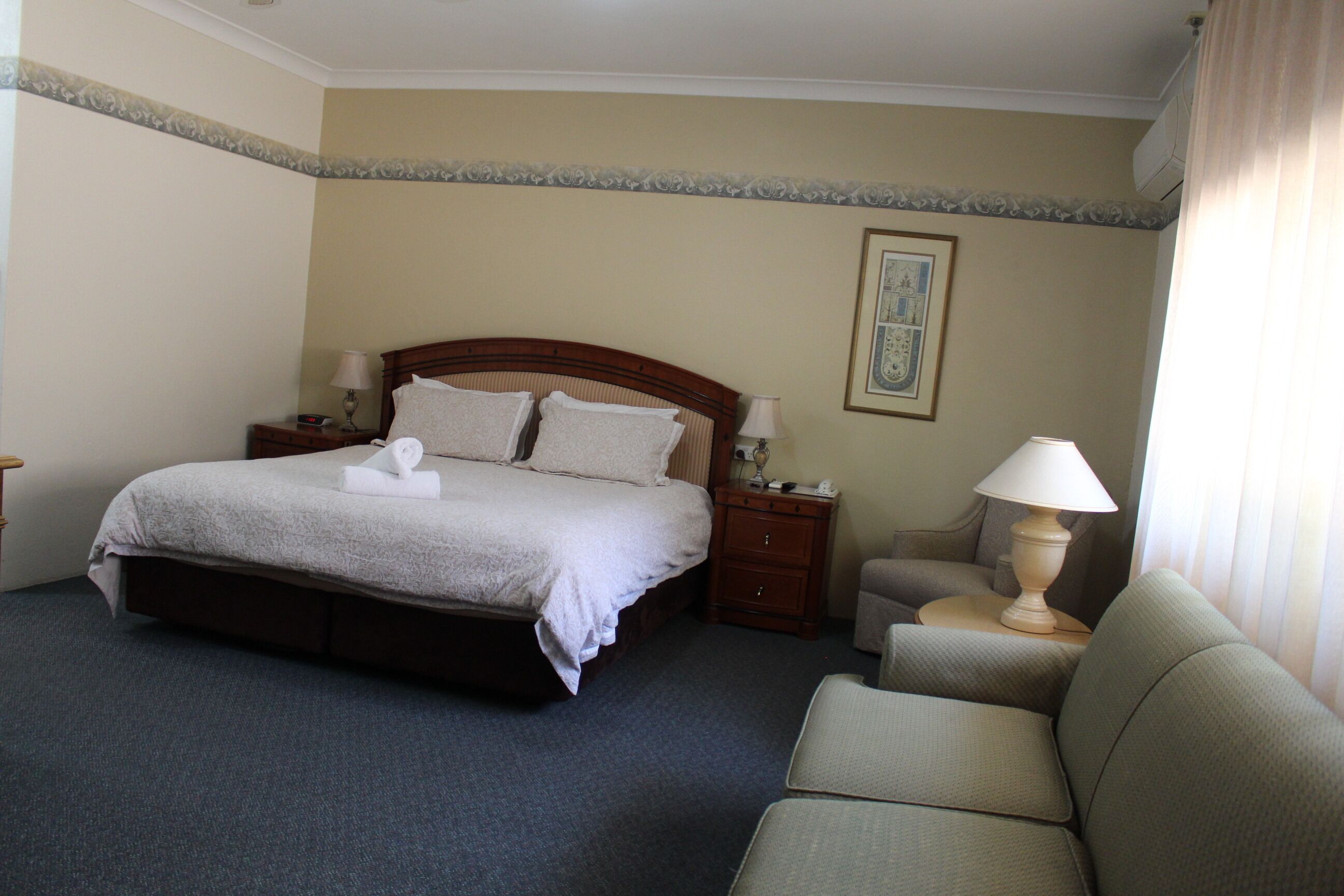 A hotel room with a bed, bedside tables, a lamp, and a chair.
