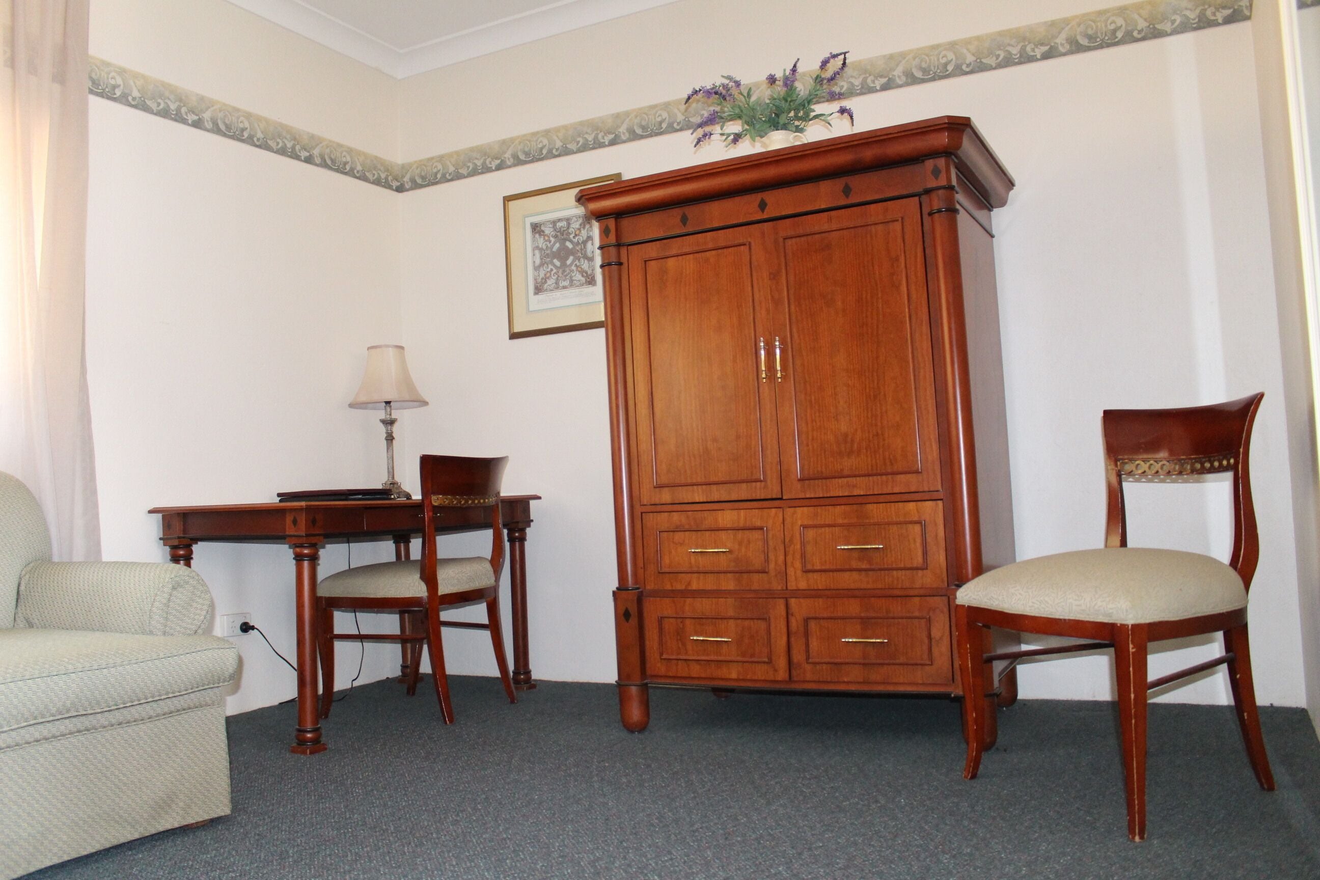Una habitación con un armario de madera, un escritorio con lámpara, una silla y un sofá.