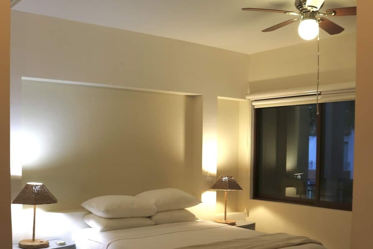 Een slaapkamer met een bed, twee bedlampen, een plafondventilator, een raam en een nachtkastje.