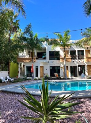 Un moderno edificio de dos pisos con piscina, rodeado de palmeras y mobiliario exterior.