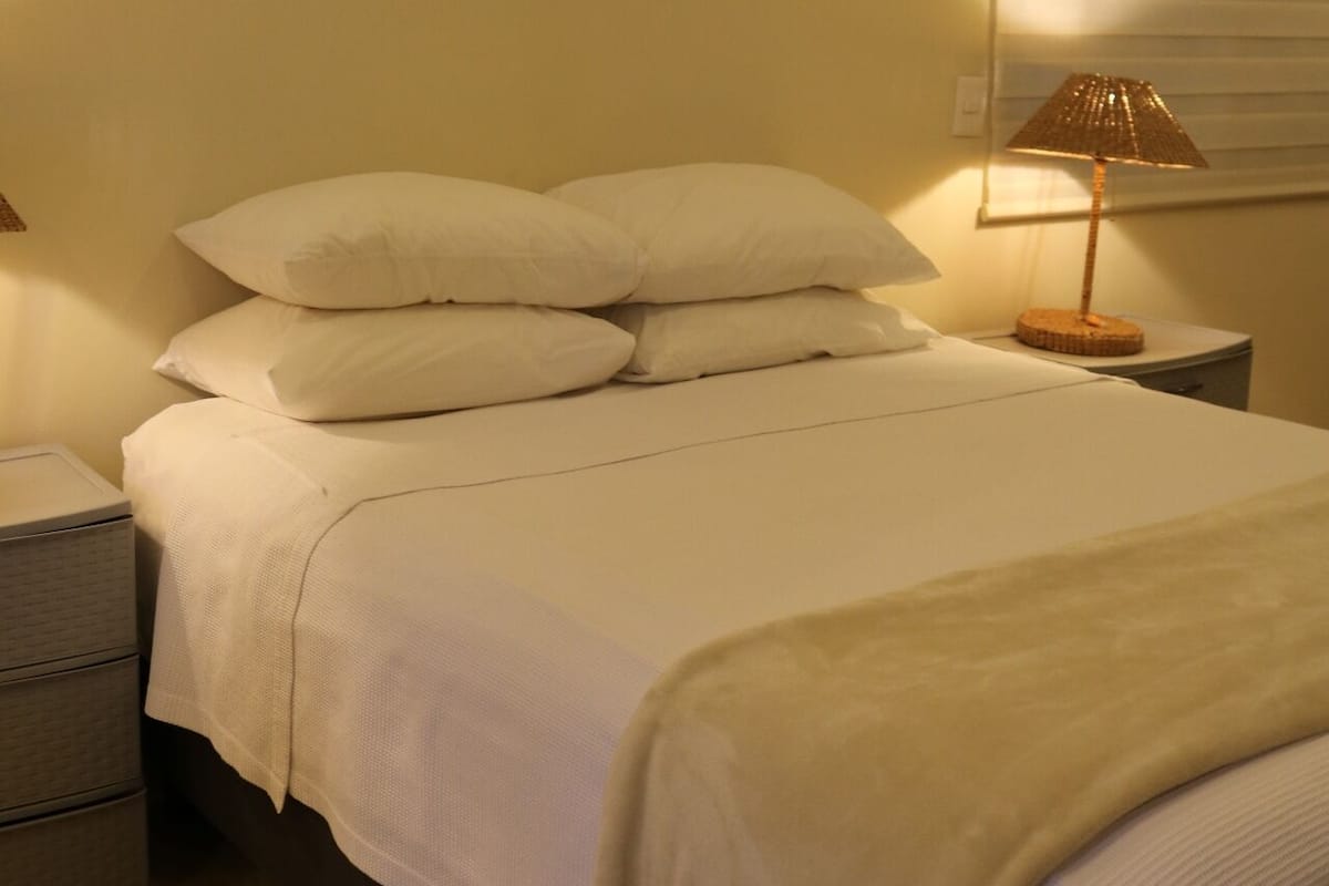 Een net opgemaakt bed met witte lakens en een lamp op een nachtkastje.