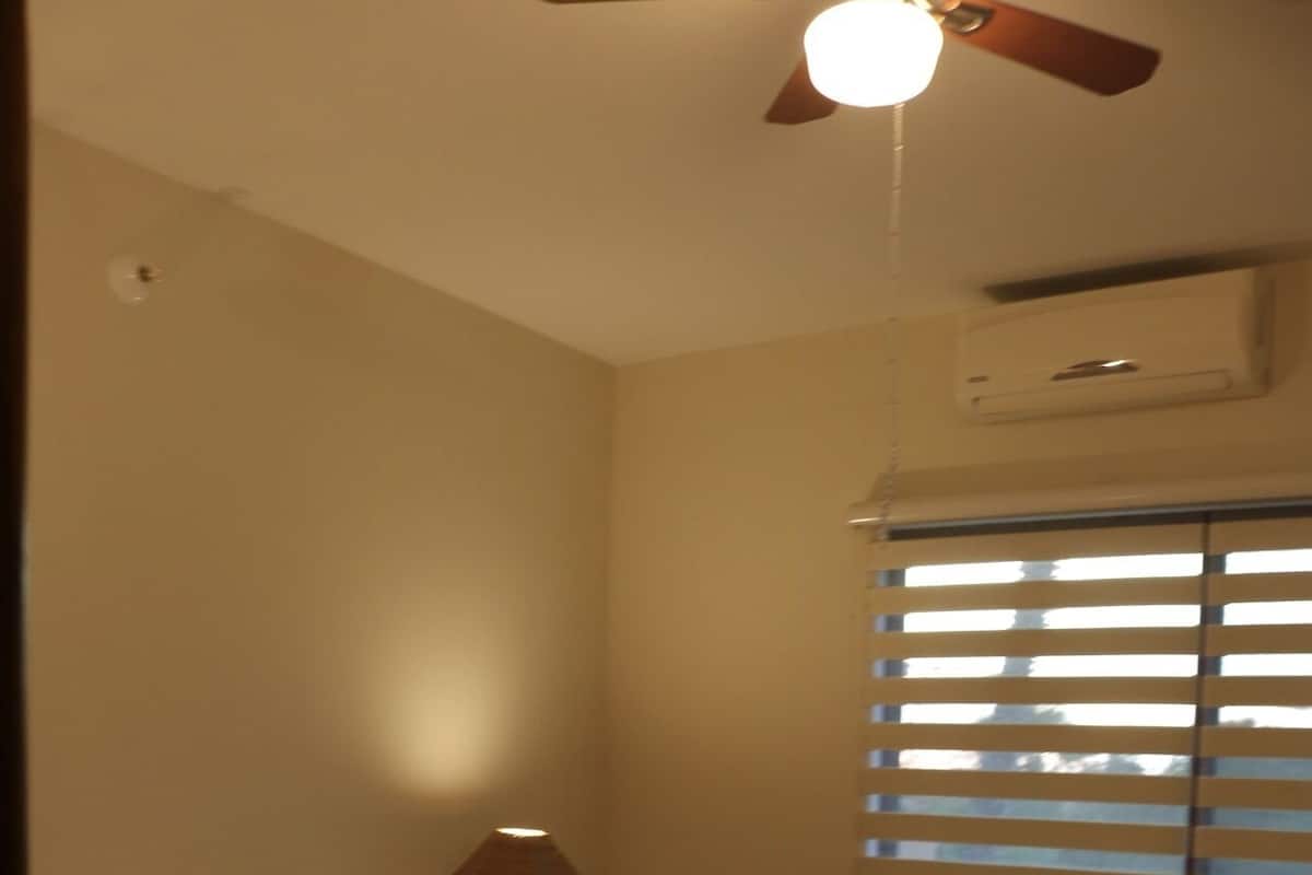Een slaapkamer met een bed, nachtkastje, lamp en plafondventilator.