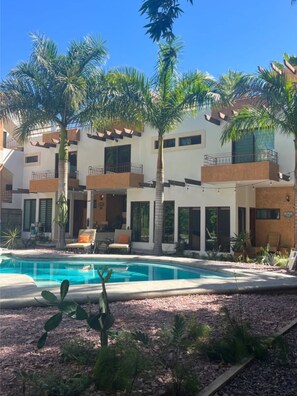Un edificio de varios pisos con piscina, palmeras y asientos al aire libre.