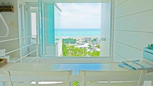A room with a large window offering a view of the ocean and a cityscape. - Coral garden 7 pools (Yomitan)