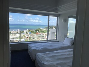 A hotel room with a large window offering a view of the sea and buildings.