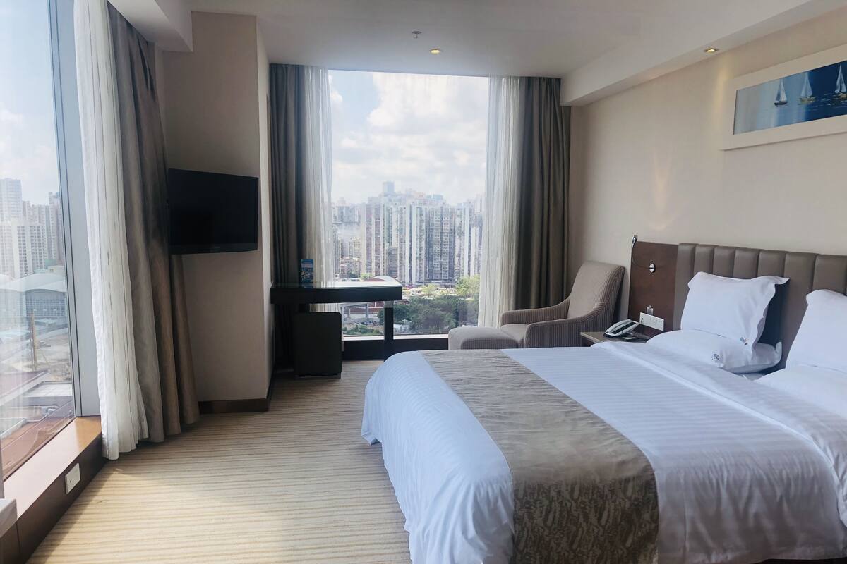 A hotel room with a large bed, a desk, a chair, and a TV.