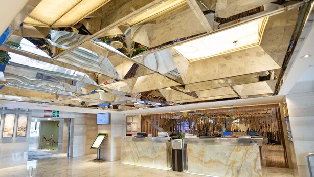 A modern lobby with a marble reception desk, a digital information screen, and a high ceiling with geometric patterns. - L Hotel Changsheng (Zhuhai)