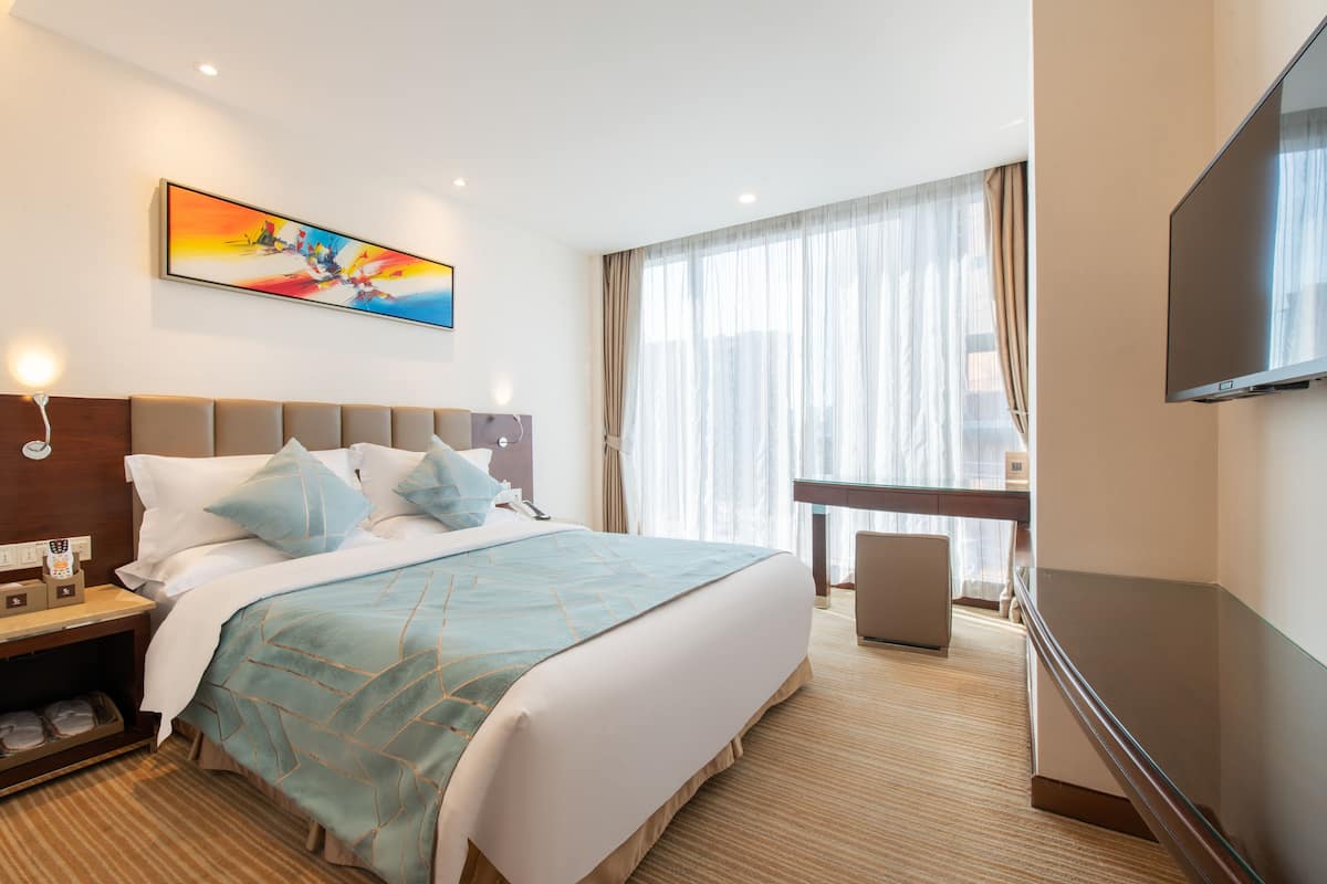 A hotel room with a large bed, a desk, a flat-screen TV, and a window with curtains.