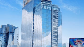 A modern hotel building with a glass facade and the name "L HOTEL" prominently displayed at the top.