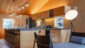 A modern kitchen with wooden cabinetry, a bar area with stools, and a large window providing natural light.