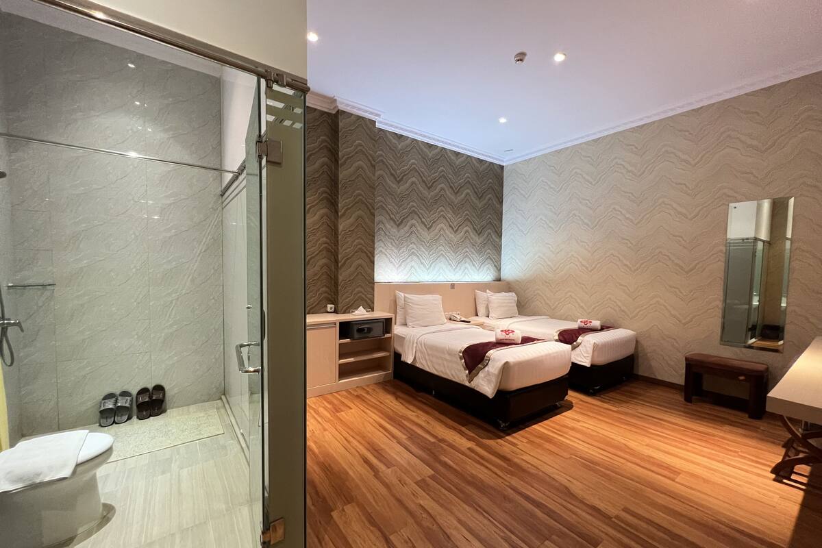 Une chambre d’hôtel avec une douche, deux lits, une table de chevet, un miroir et un plancher en bois.