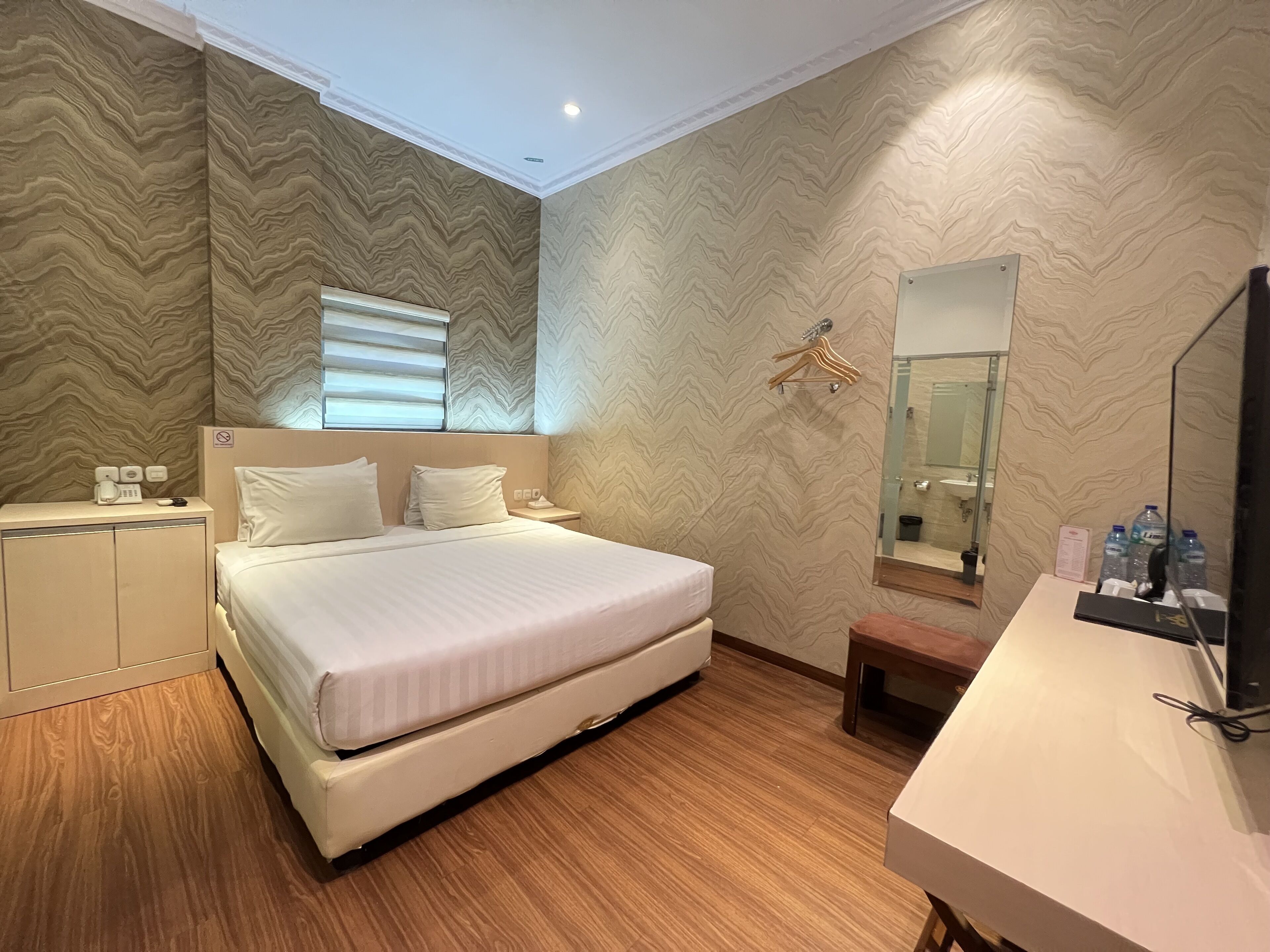 A modern hotel room with a large bed, a bedside table, a mirror, and a wooden floor.