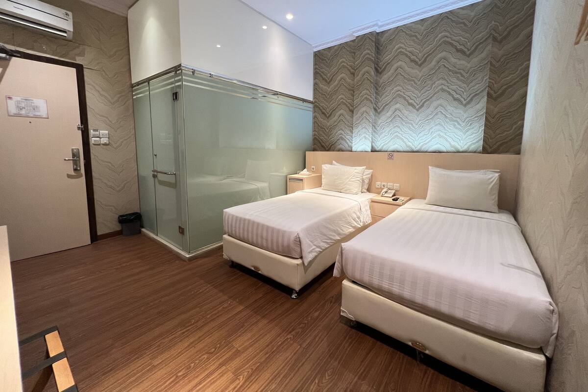 Une chambre d’hôtel avec deux lits, une douche en verre, un plancher en bois et un mur à motifs.