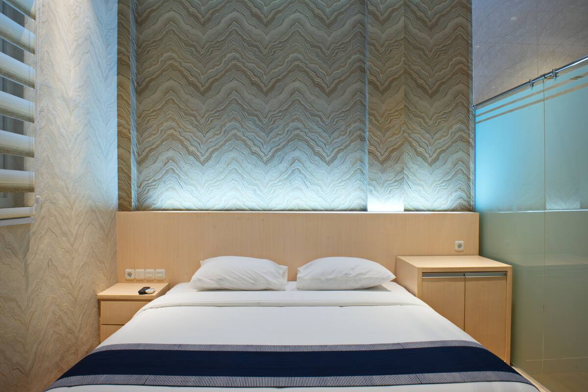 Une chambre d’hôtel moderne avec un grand lit, une tête de lit en bois et un mur décoré d’un motif au-dessus du lit.