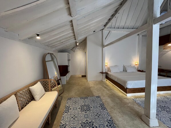 A bedroom with a bed, a bedside table, a mirror, a sofa, and a patterned rug.