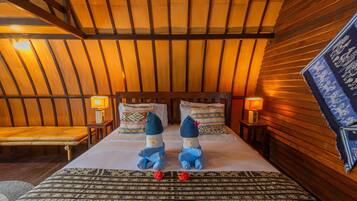 Una habitación acogedora con techo inclinado de madera, una cama con dos almohadas, una mesita de noche con lámpara y una alfombra estampada.
