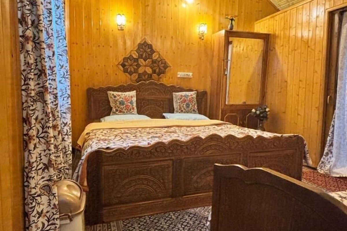 A bedroom with a wooden ceiling, a large bed with patterned bedding, a nightstand, and a mirror.