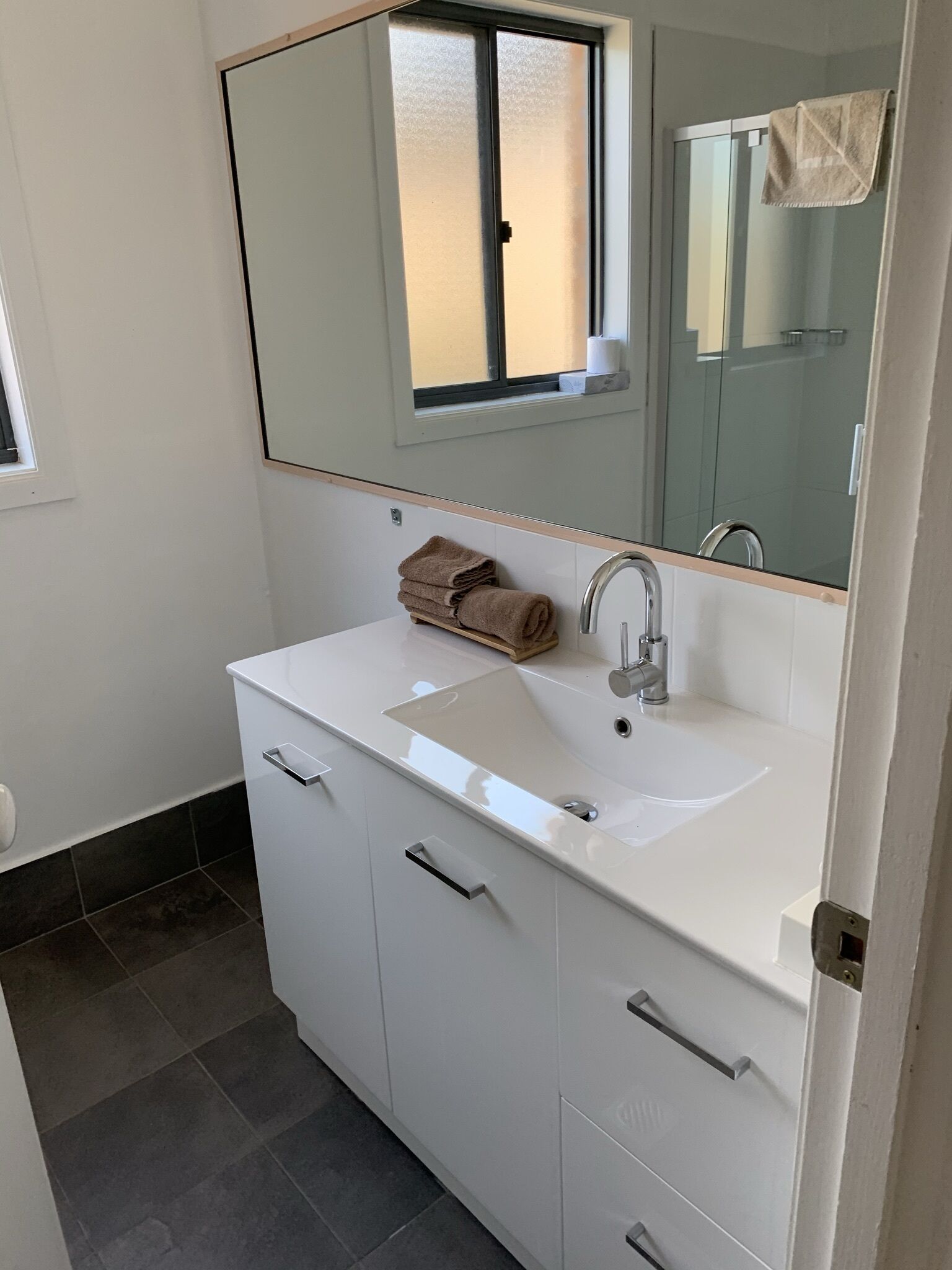 Un baño con un lavamanos blanco, un espejo encima y una toalla en la encimera.