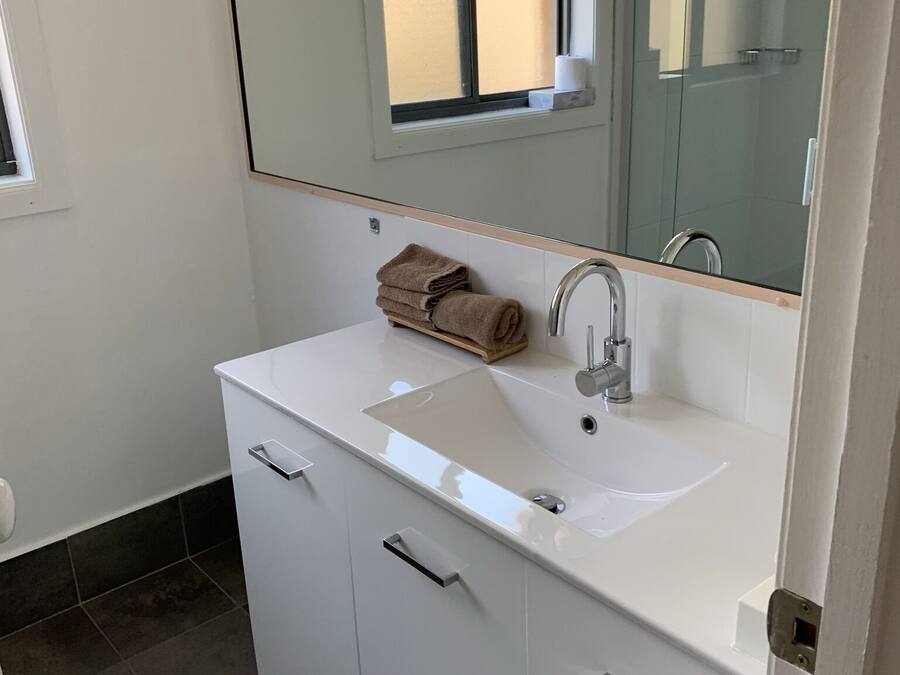 Un baño con un lavamanos blanco, un espejo encima y una toalla en la encimera.