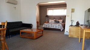 A living room with a black sofa, wooden coffee table, and a bed with patterned bedding. - Swaggers Motor Inn (Yass)