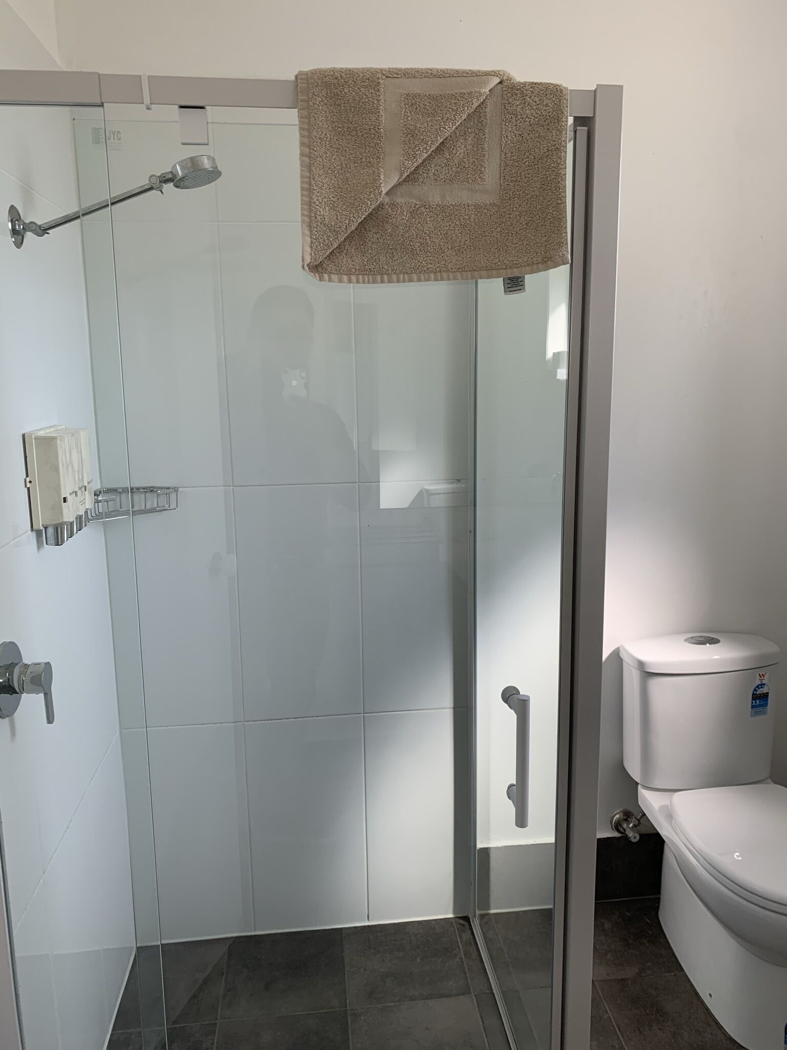 Doccia vetrata con un asciugamano appeso alla porta, un water e un piccolo ripiano con articoli da toilette.