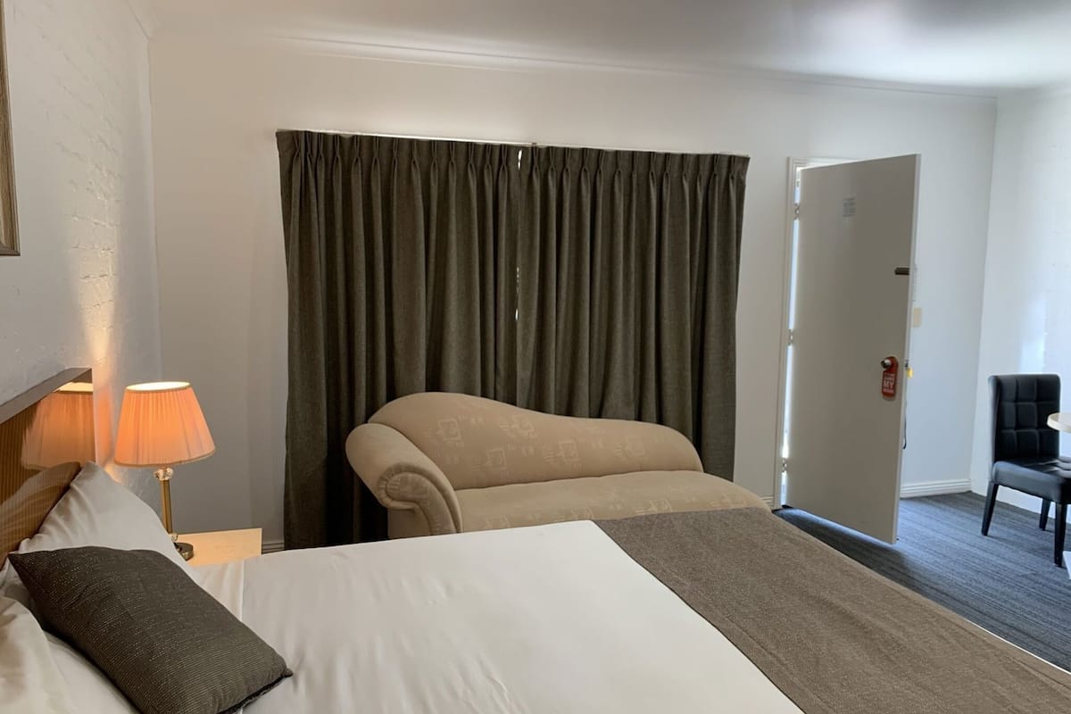 A hotel room with a bed, a chair, a lamp, and a door.