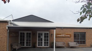 A brick building with a sign reading "Swagger's Conference Centre." There are two doors, a bench, and a chair outside. - Swaggers Motor Inn (Yass)