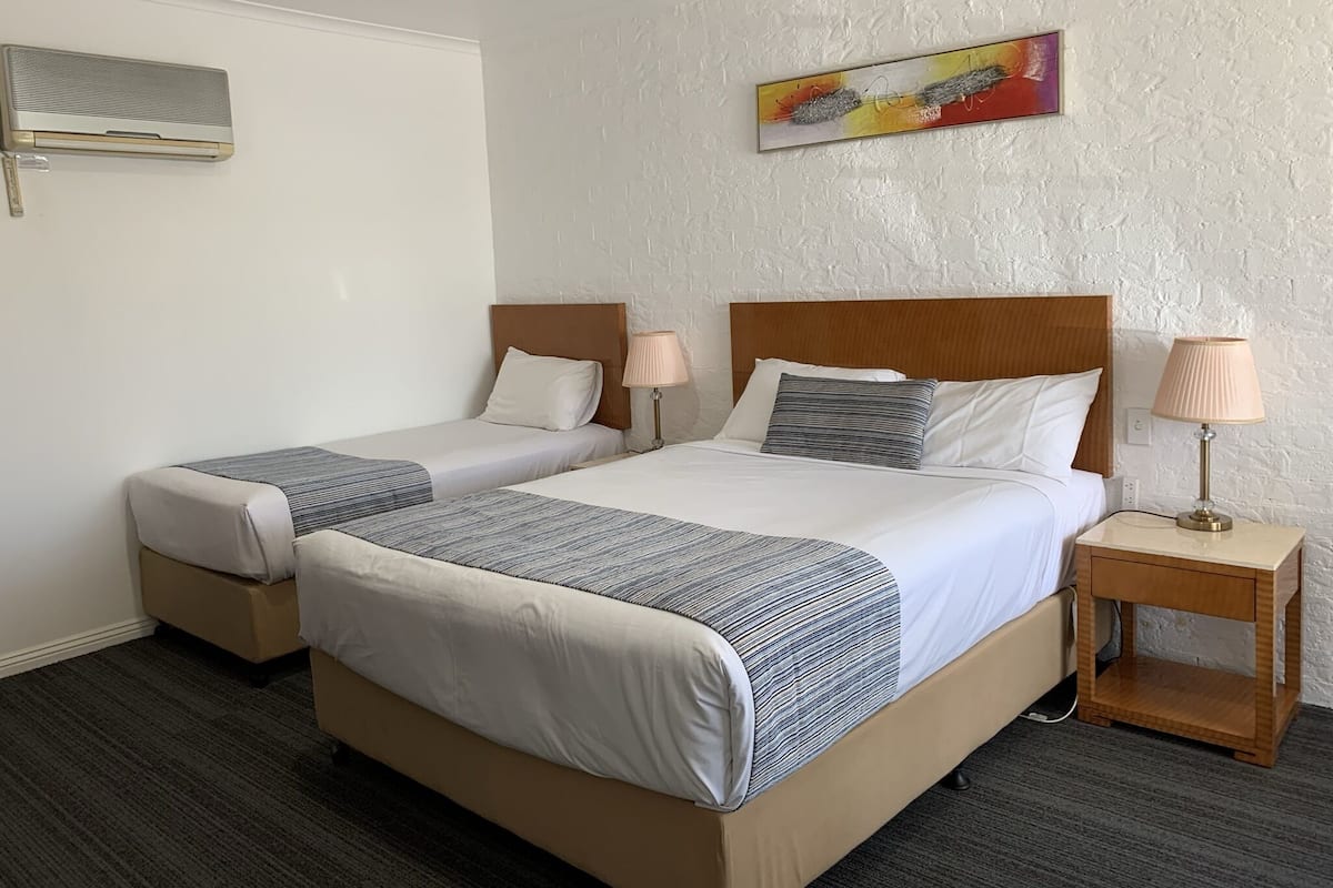 A hotel room with two beds, each with a wooden headboard, a bedside table with a lamp, and a painting on the wall.