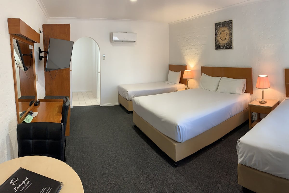 A hotel room with two beds, a desk with a chair, a TV mounted on the wall, and an air conditioning unit.