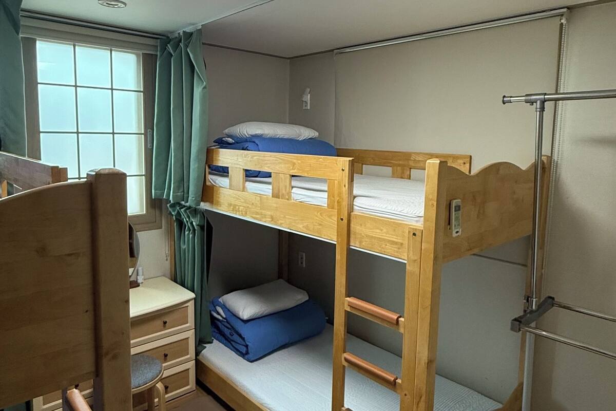 Une chambre avec un lit superposé, un bureau, une chaise et une fenêtre avec des rideaux.