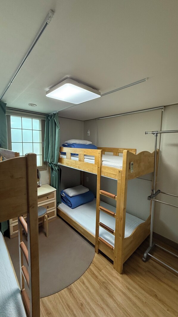A bunk bed room with a desk, chair, and a window with curtains.