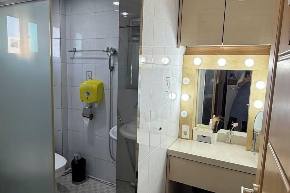 A bathroom with a toilet, sink, and mirror with lights.