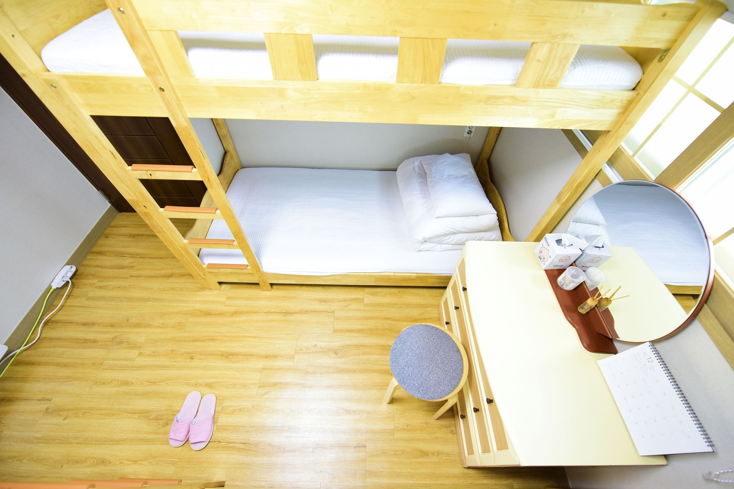 A bunk bed room with a desk, mirror, and a small stool.