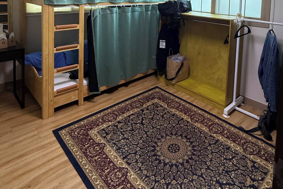 Une chambre avec un lit superposé, un bureau, une chaise, une fenêtre avec des rideaux, un radiateur et un tapis à motifs.
