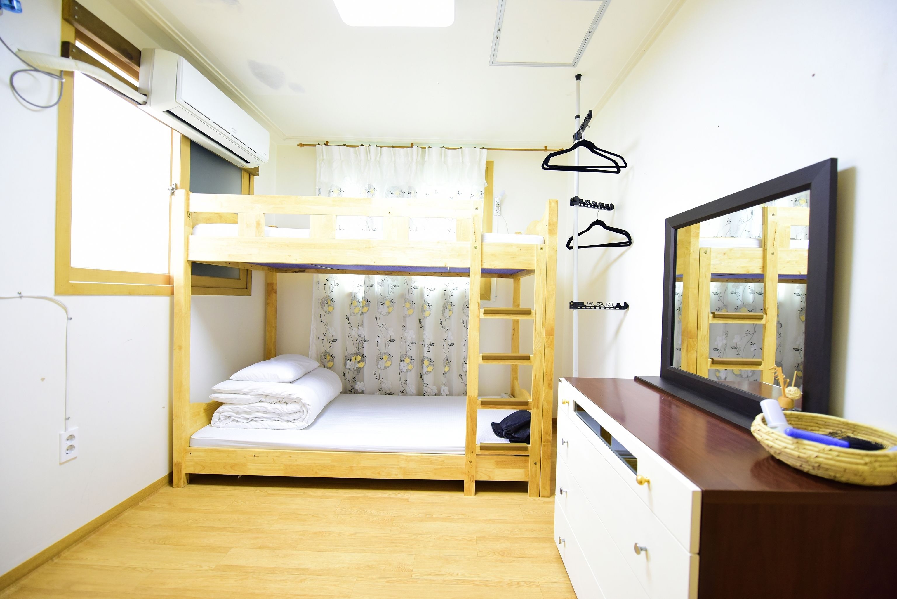 A bunk bed room with a wooden desk, a mirror, and a hanging clothes rack.