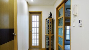 Un couloir avec un plancher en bois, une porte en bois, une porte en verre et un téléphone fixé au mur.