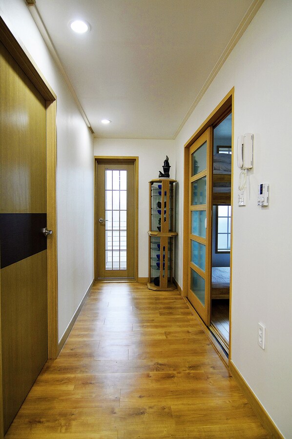 A hallway with wooden flooring, a wooden door, a glass door, and a telephone on the wall.