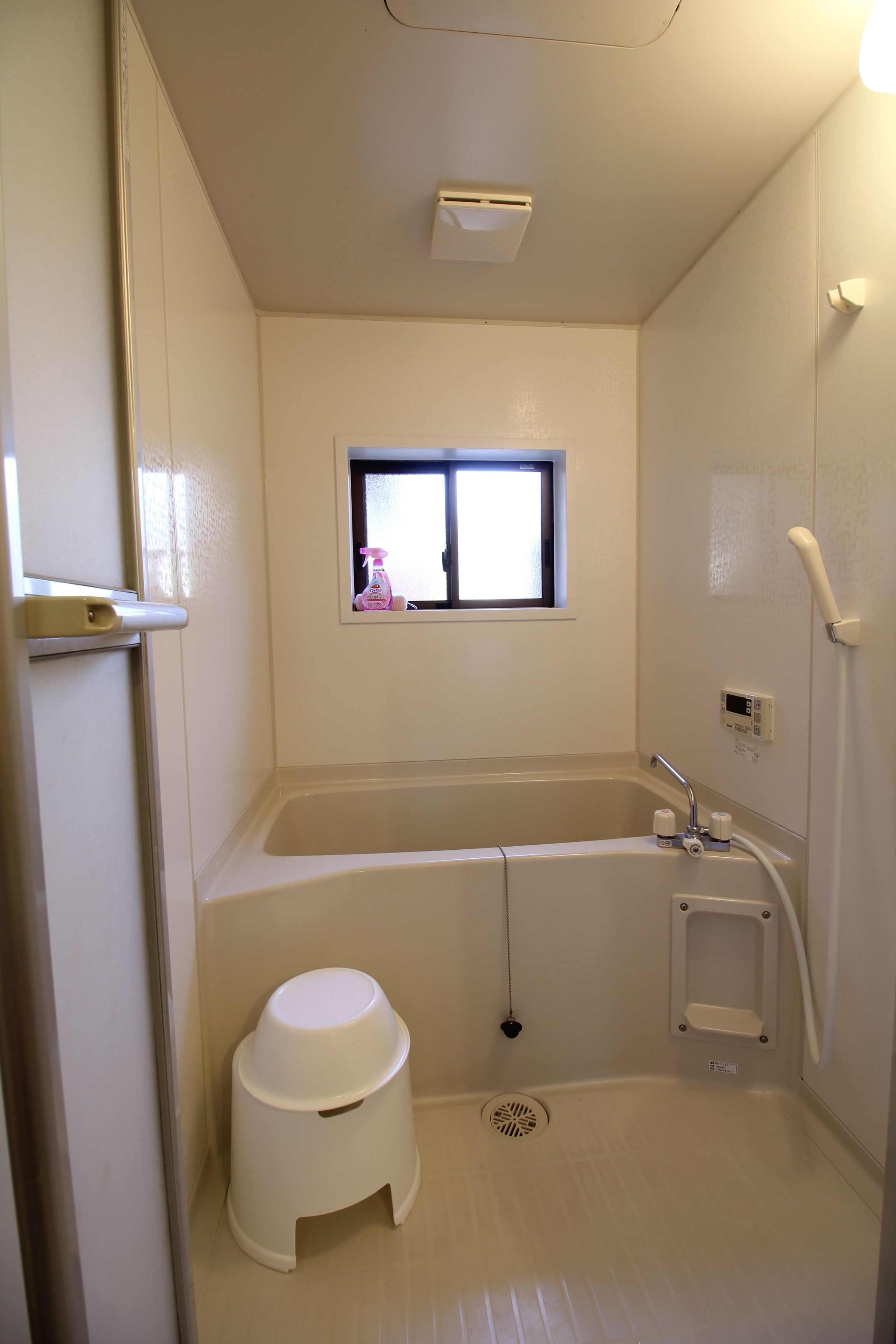 Un baño pequeño y blanco con bañera, ventana, inodoro y ducha.