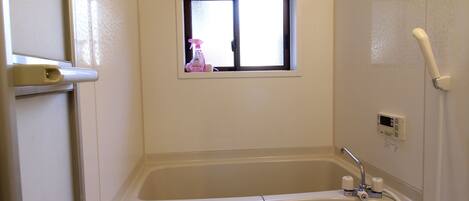 Un baño pequeño y blanco con bañera, ventana, inodoro y ducha.