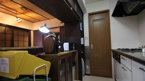 A kitchen with a wooden cabinet, a microwave, and a stove. There is a door on the right side. - JQ Villa Kyoto Maiko Han-Inn (Kyoto)