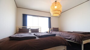 A room with two beds, a window with blue curtains, and a hanging light fixture. - JQ Villa Kyoto Maiko Han-Inn (Kyoto)