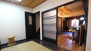 A room with tatami mats, a woven stool, a sliding door, and a kitchen area with stools and a table. - JQ Villa Kyoto Maiko Han-Inn (Kyoto)